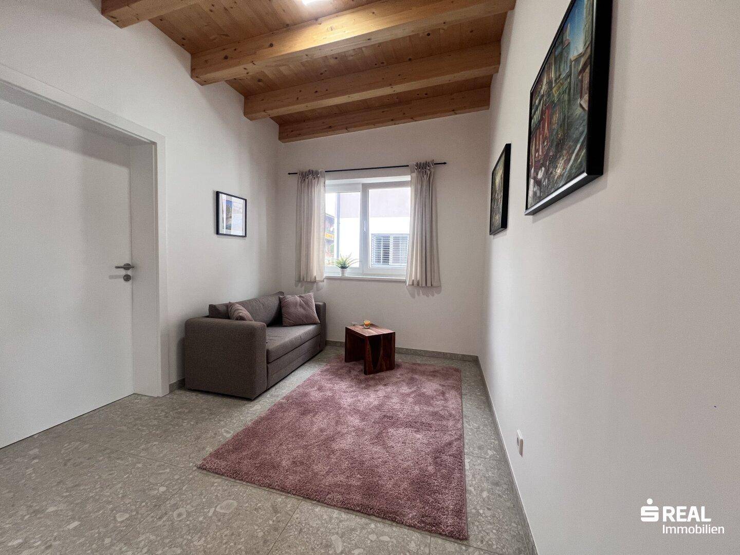 Kleiner Wohnbereich mit Sofa, Teppich und Holzbalkendecke.
