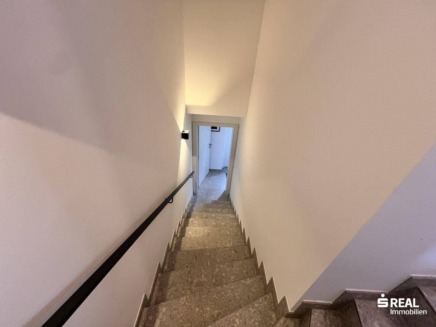 Treppenhaus mit gefliesten Stufen und Handlauf, führt in den unteren Bereich.