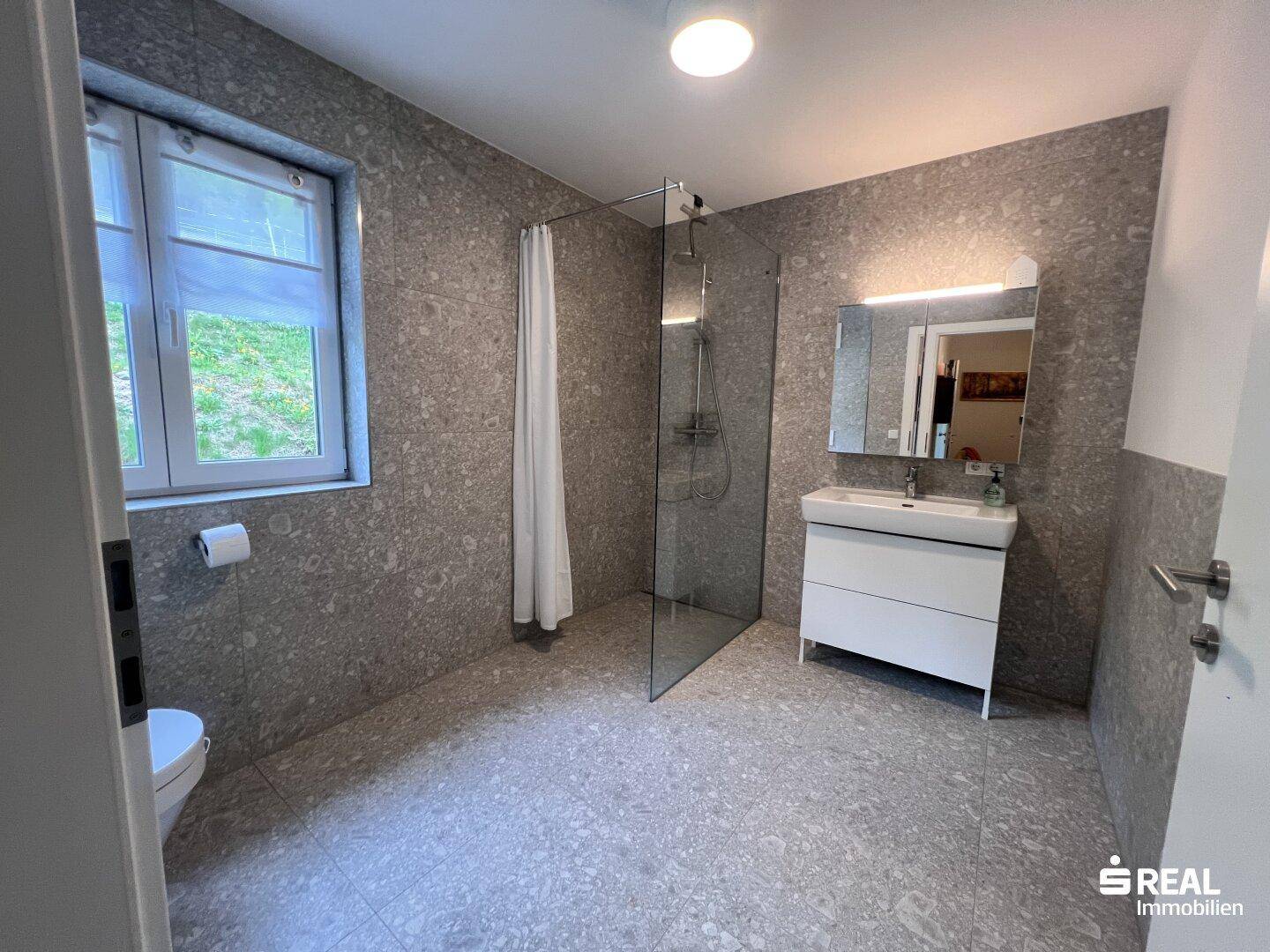 Helles Badezimmer mit Toilette, begehbarer Dusche und Fenster.