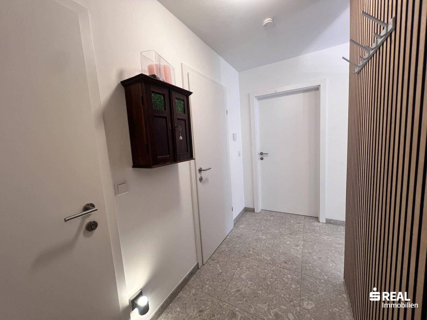 Eingangsbereich mit Garderobe, kleinem Schrank und Fliesenboden.