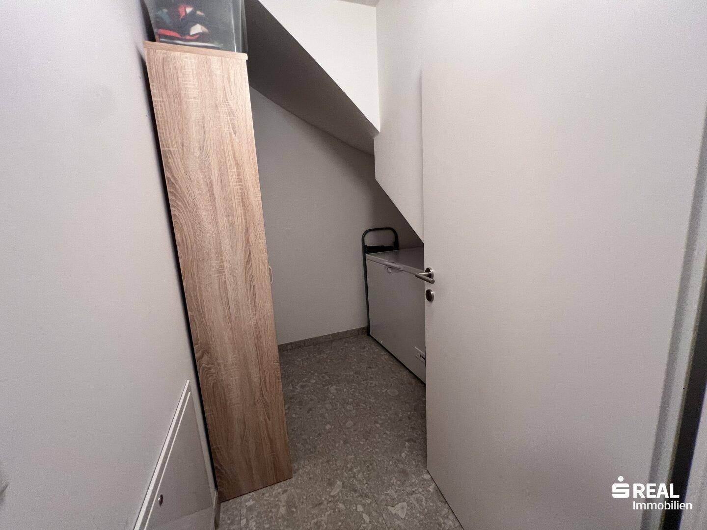 Kleiner Abstellraum unter der Treppe mit Regal und Gefrierschrank.