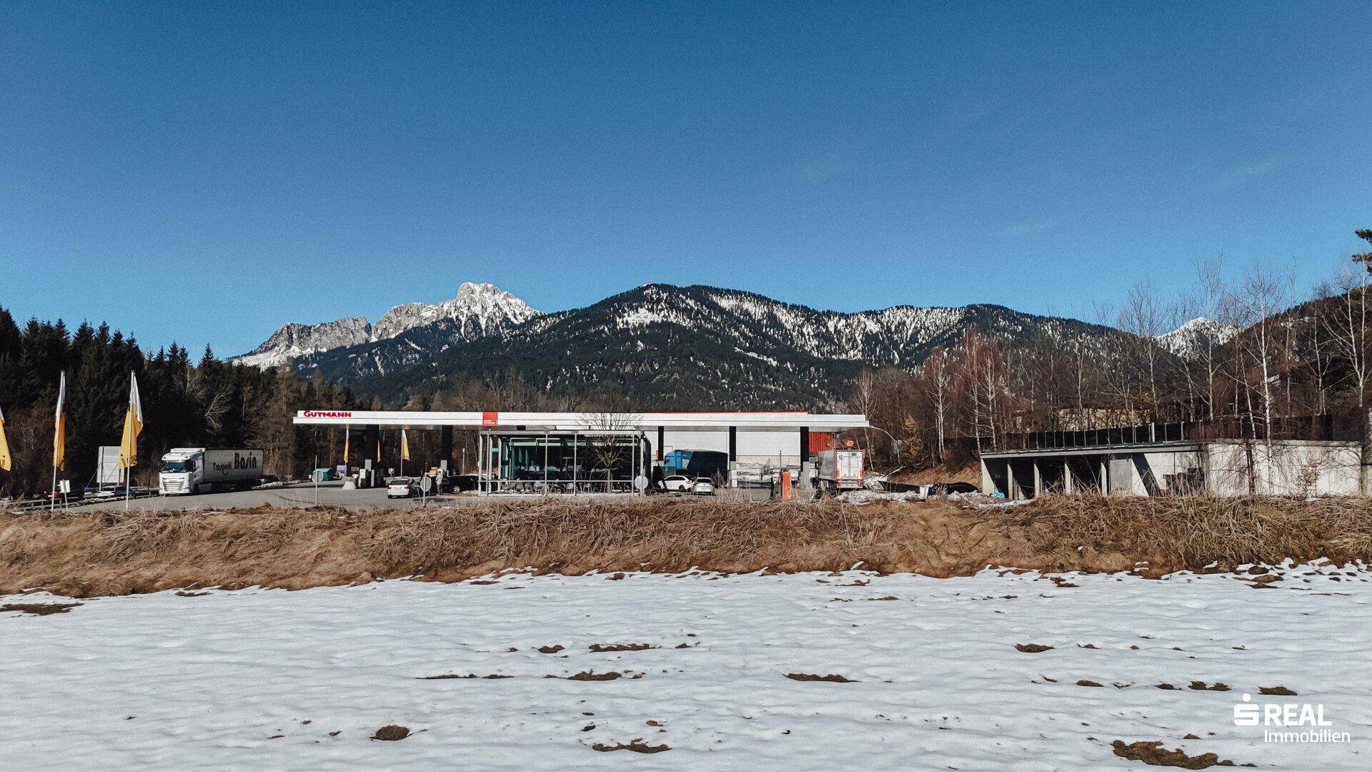 Tankstelle vor einem verschneiten Feld mit einer beeindruckenden Bergkulisse im Hintergrund.