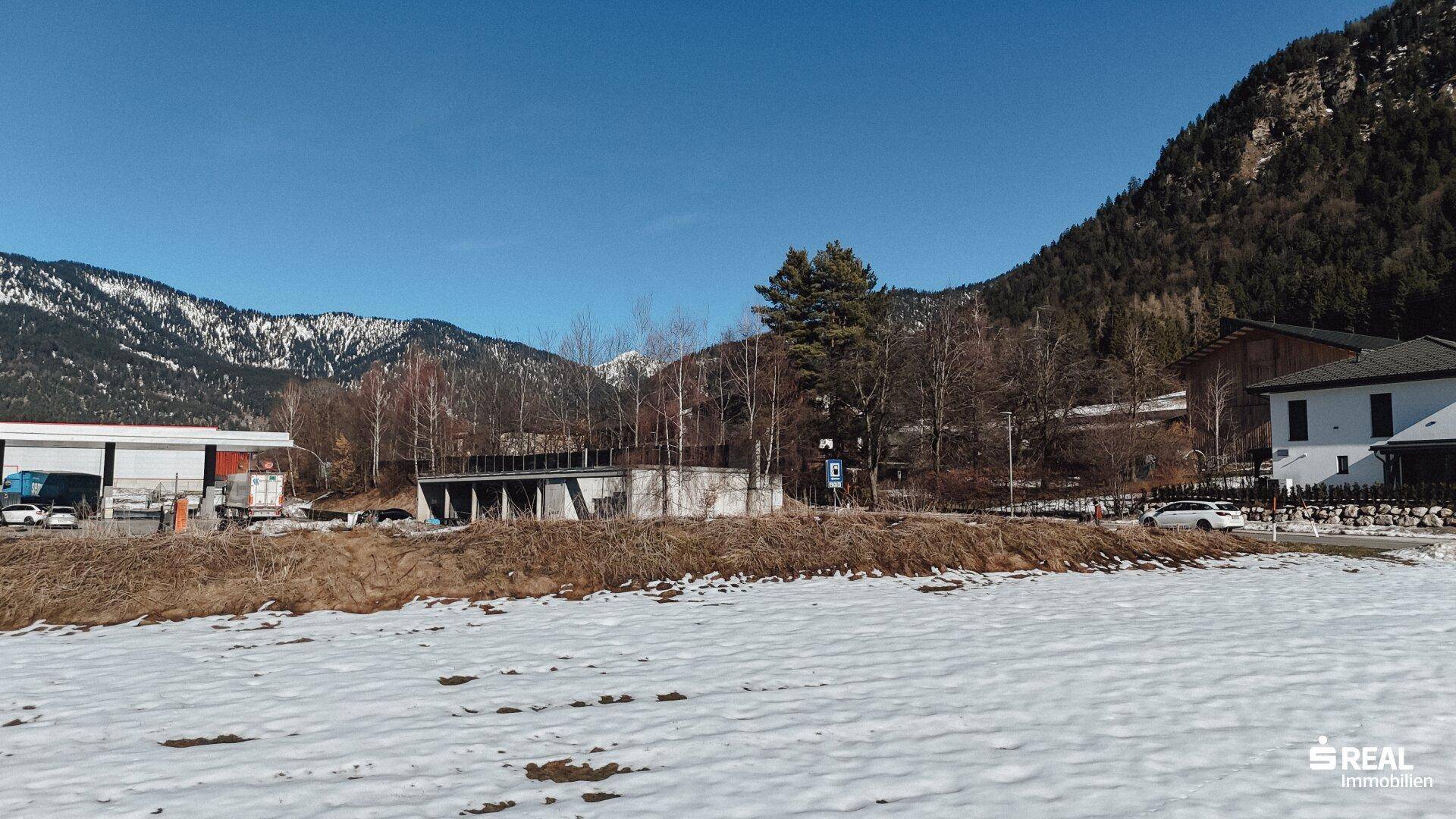 Verschneite Landschaft mit Gebäuden und einer Bergkette unter klarem blauem Himmel.