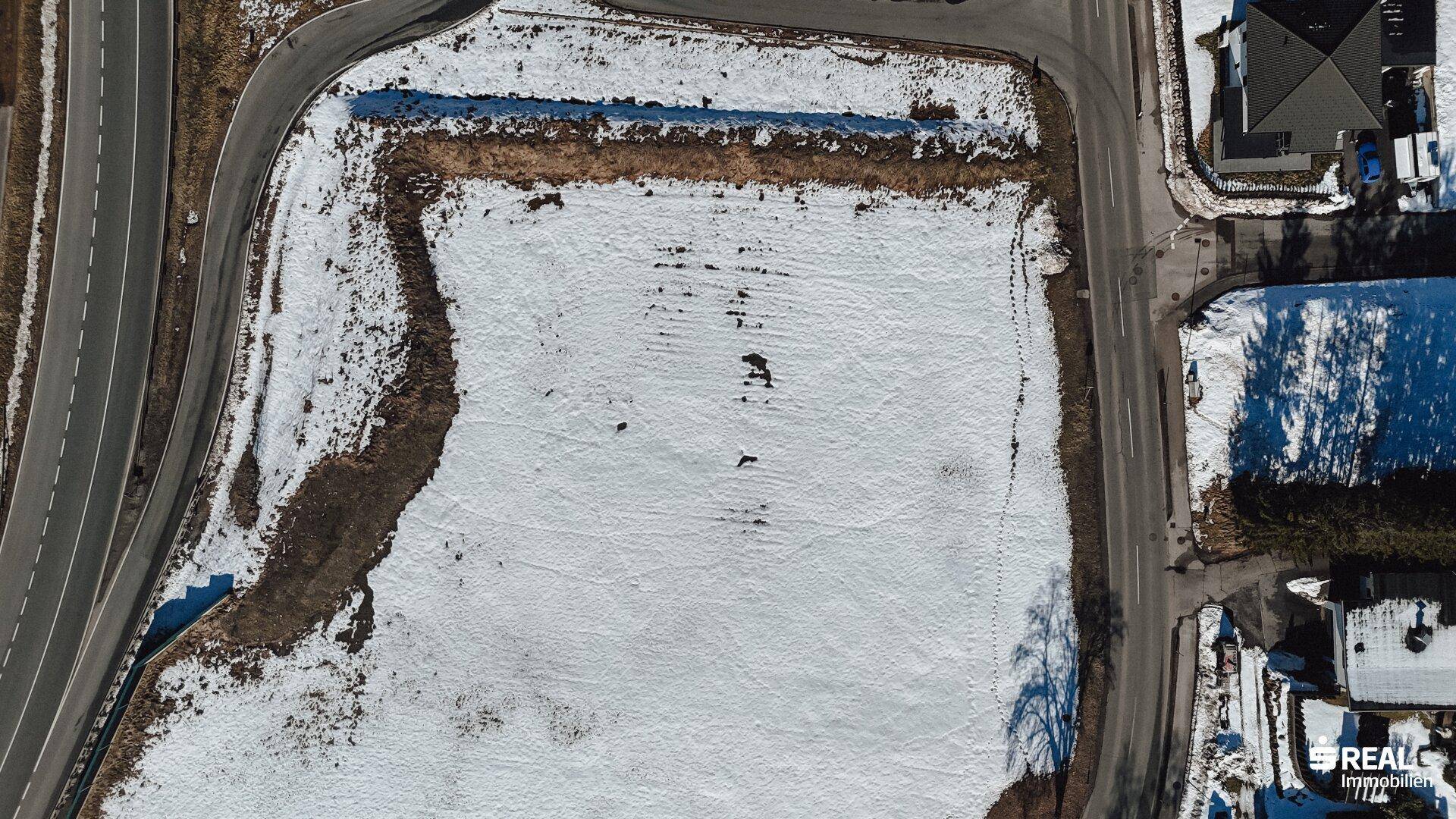 Luftbild zeigt ein großes, verschneites Feld mit angrenzenden Straßen und Gebäuden.