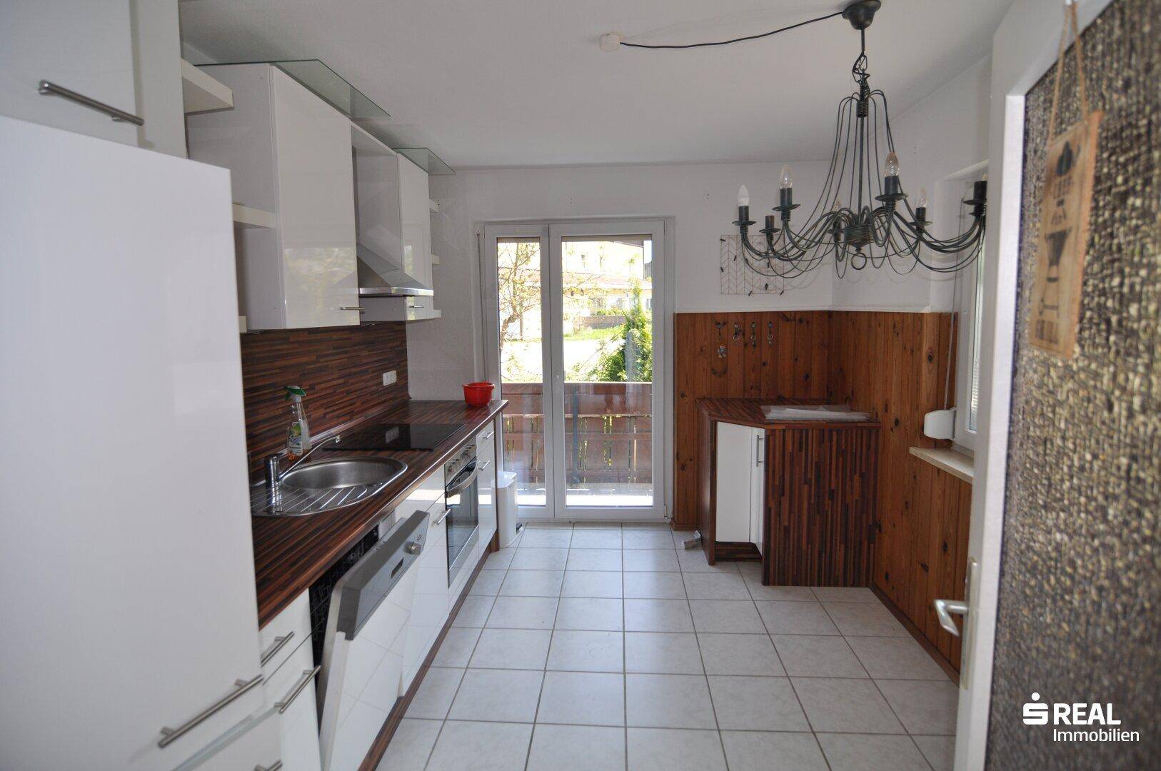 Helle Küche mit weißen Hochglanzschränken, Holzarbeitsplatte und Zugang zum Balkon.