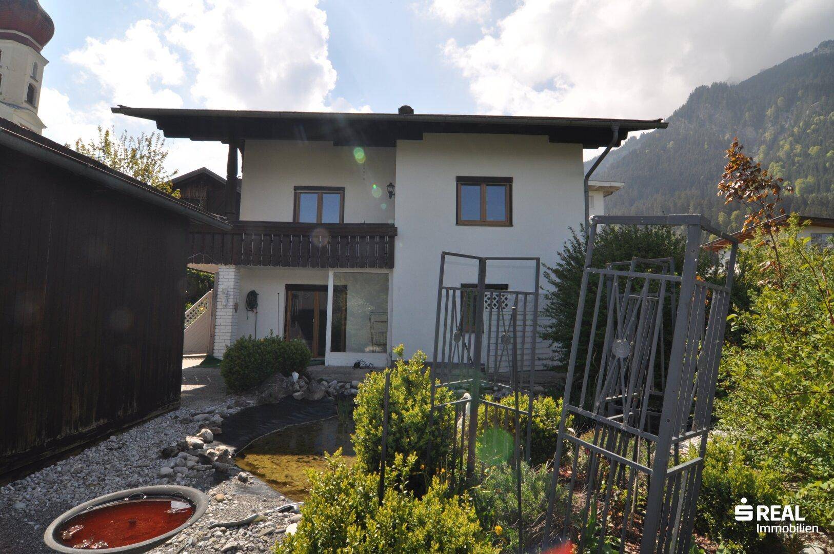 Rückseite eines Hauses mit kleinem Teich, Gartenbereich und Blick auf die Berge.