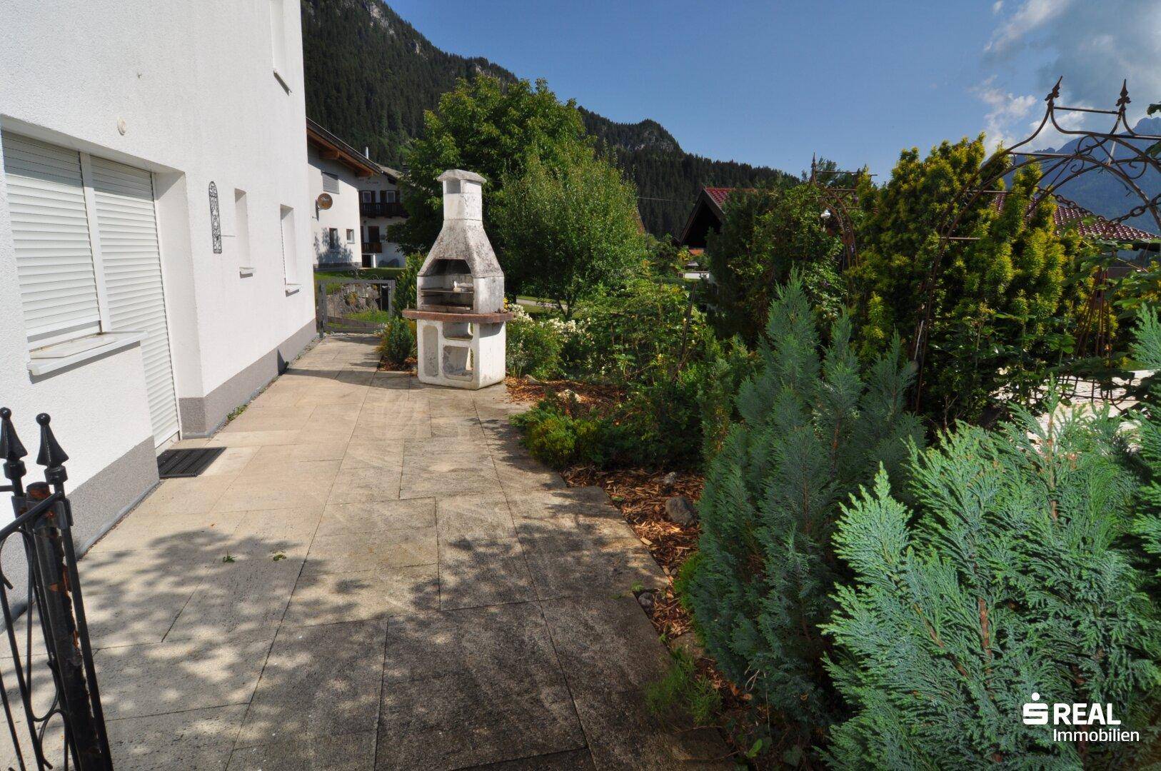 Gepflasterter Außenbereich mit festem Grillplatz und umgebender Bepflanzung.