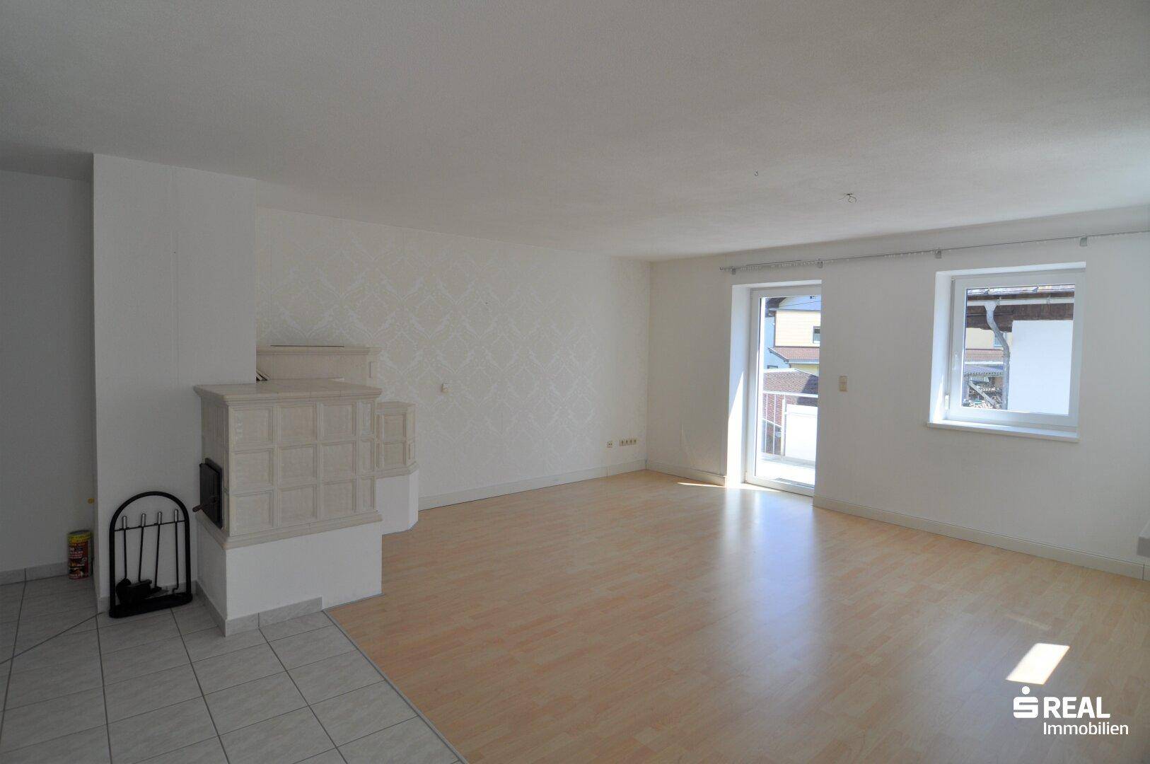 Gemütliches Wohnzimmer mit Kachelofen, Laminatboden und Zugang zu einem Balkon.