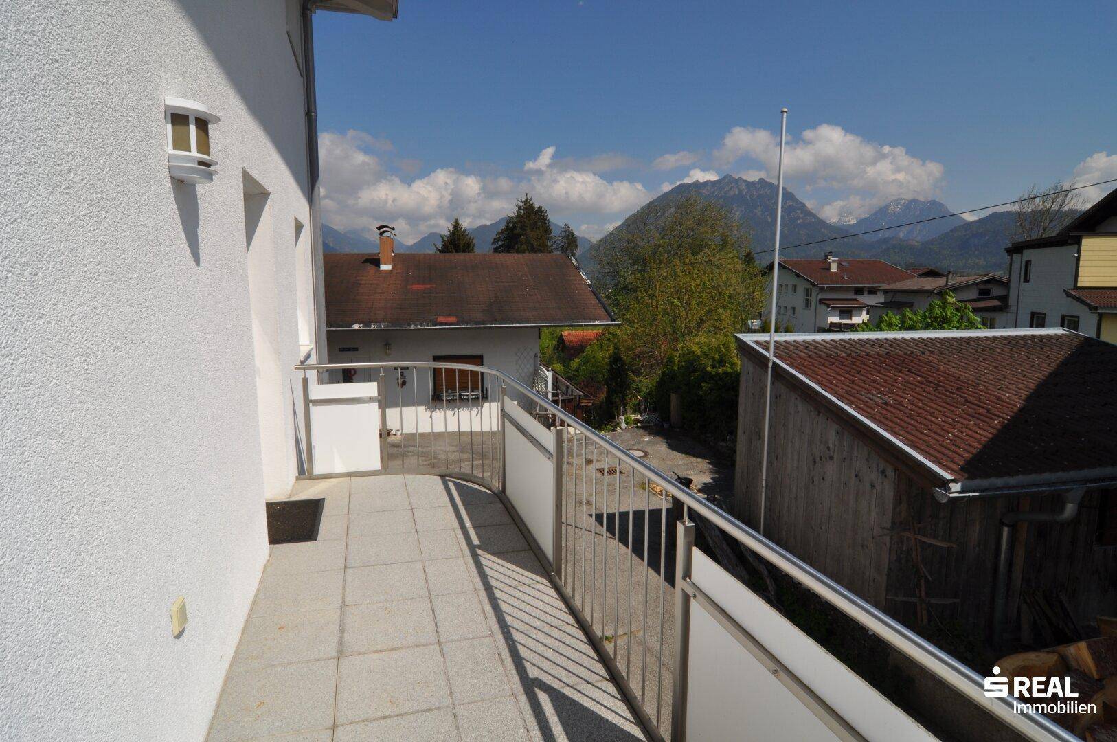 Geräumiger Balkon mit Fliesenboden, Metallgeländer und weitem Blick auf die Berge.