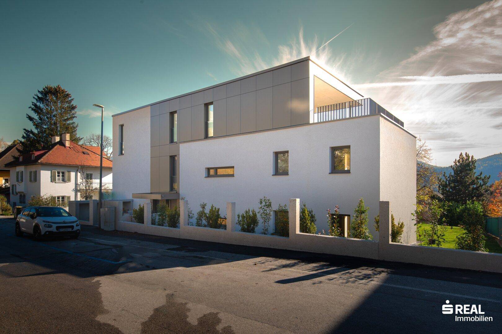 Moderne Architektur mit weißer Fassade und Dachterrasse unter strahlendem Himmel.