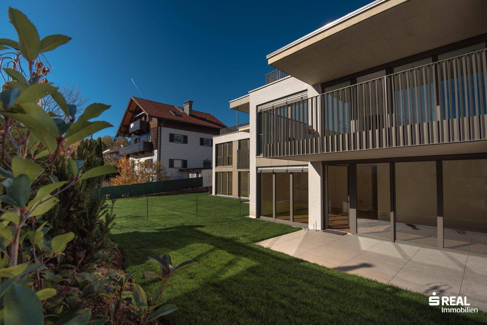 Gepflegter Rasenbereich mit einer Terrasse und Zugang zum modernen Gebäude unter blauem Himmel.