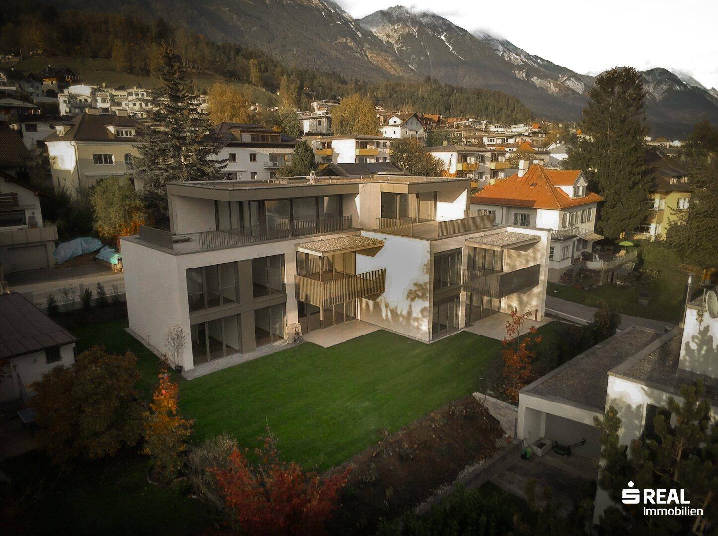 Luftaufnahme eines modernen Wohnkomplexes mit großzügigen Grünflächen und Bergblick.