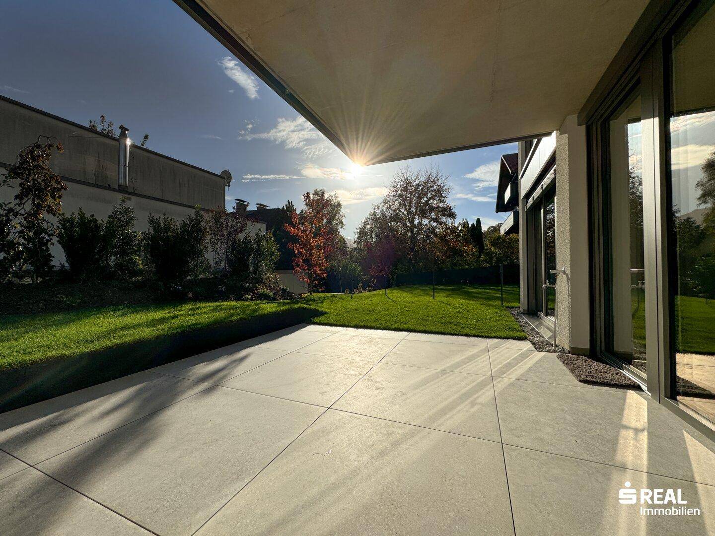 Sonniger Terrassenbereich mit großen Fliesen und direktem Zugang zum grünen Garten.