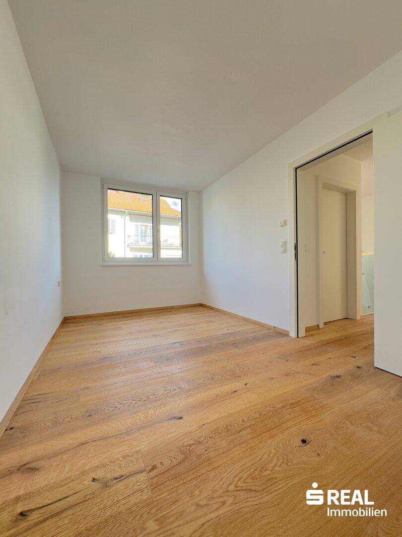 Helles Zimmer mit Holzboden und Fenster, ideal als Schlaf- oder Arbeitszimmer nutzbar.