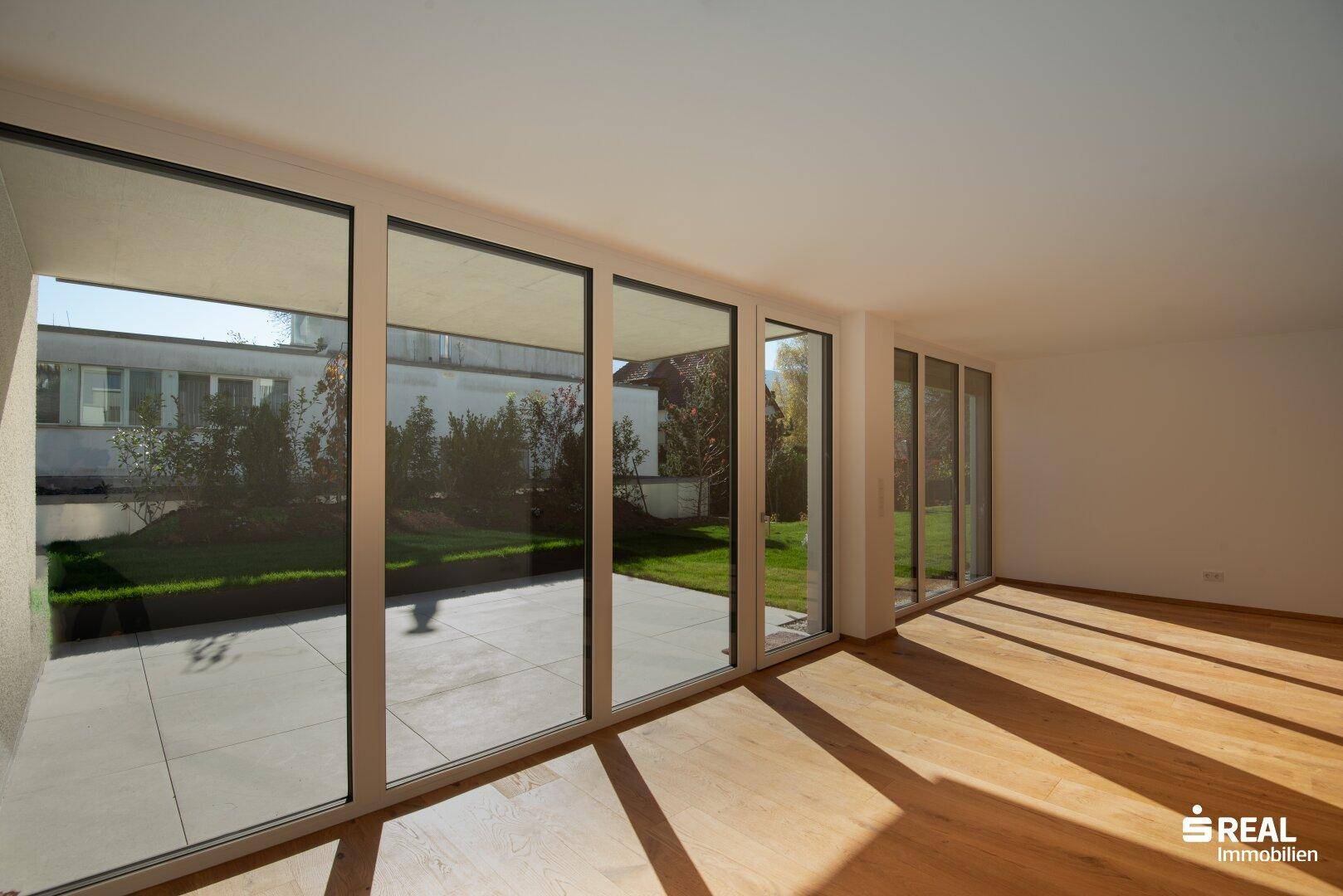 Heller Wohnraum mit Holzboden und großen Fensterfronten zum Garten und zur Terrasse.