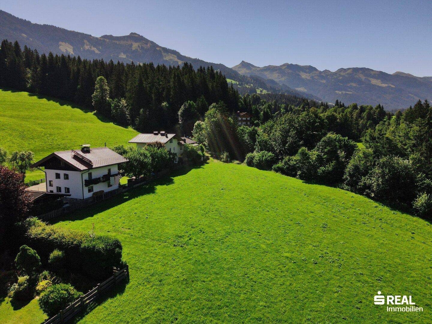 Panoramablick aus der Luft auf eine idyllische Landschaft mit Häusern, Feldern und bewaldeten Bergen.