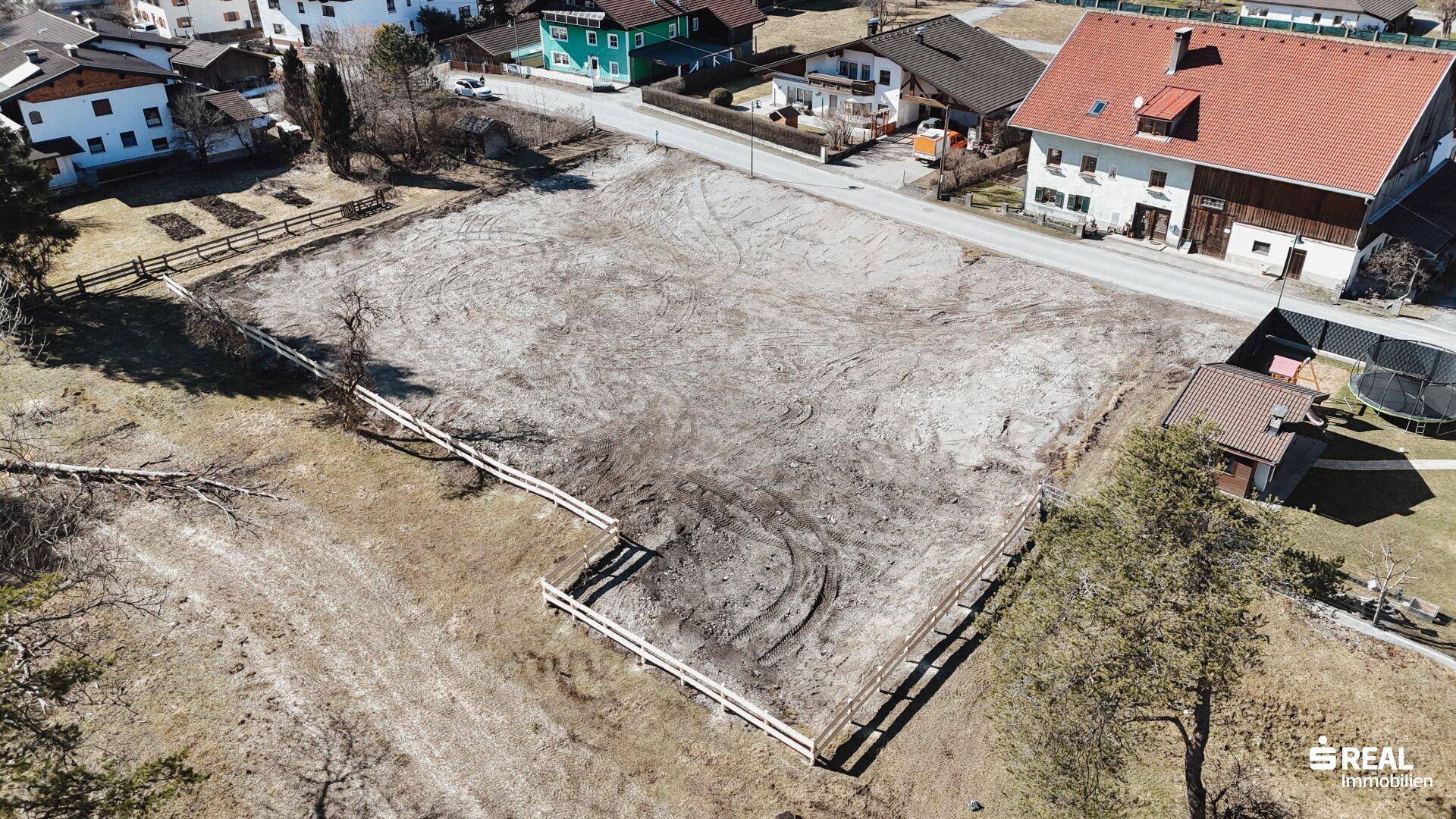Panoramablick von oben auf ein großes, eingezäuntes Grundstück, umgeben von Bäumen und einer kleinen Siedlung.
