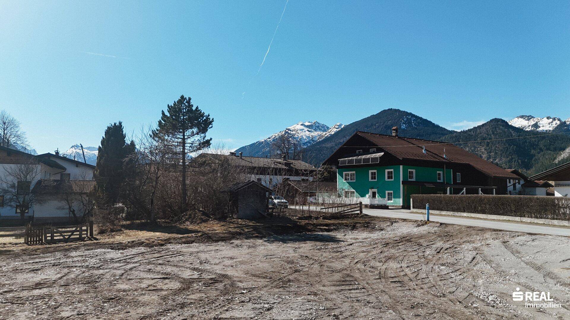 Blick vom Grundstück auf die umliegende Berglandschaft und benachbarte Häuser unter klarem blauem Himmel.