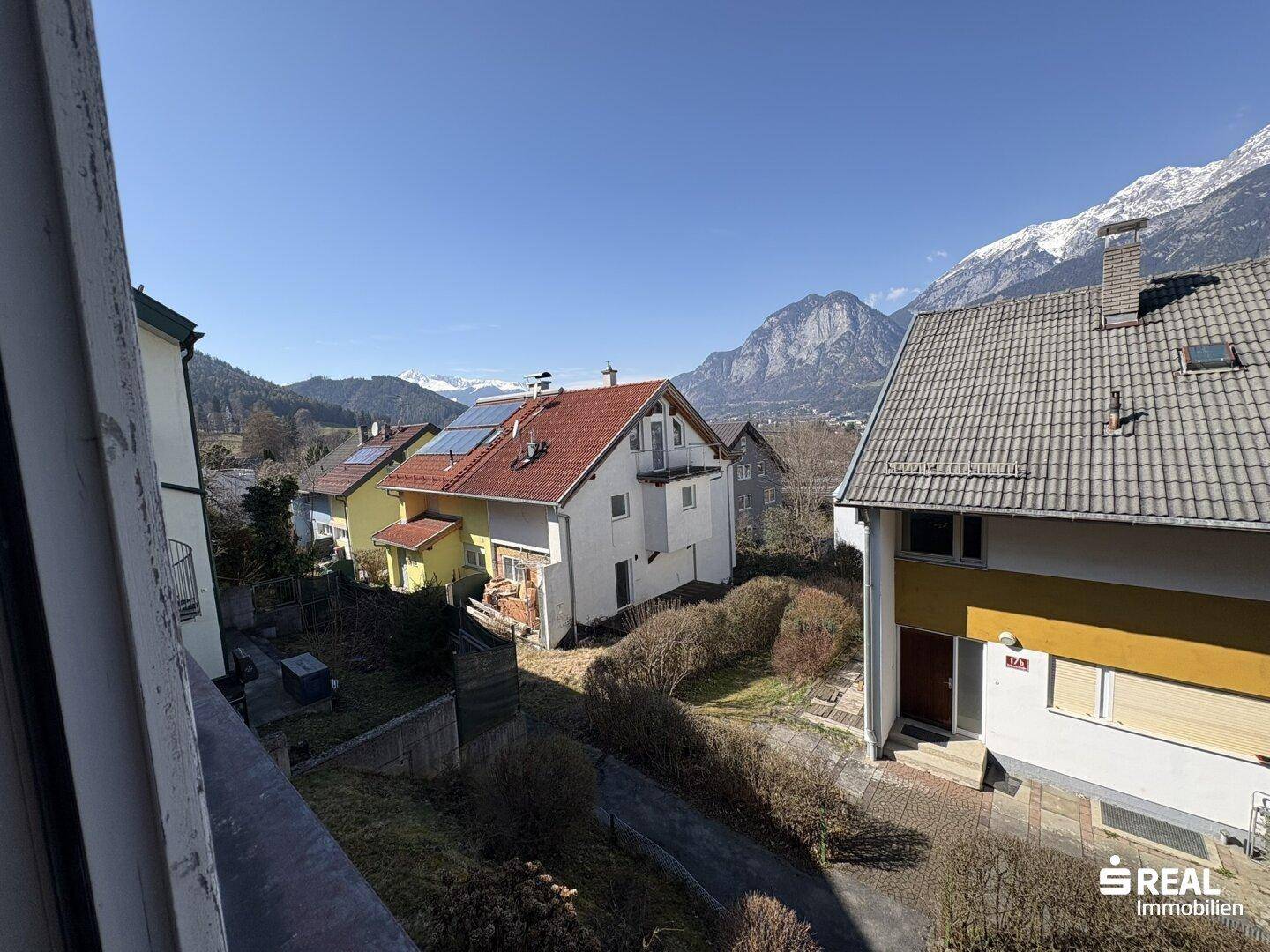 Weitblick über die Nachbarschaft mit weiteren Häusern und schneebedeckten Bergen im Hintergrund.