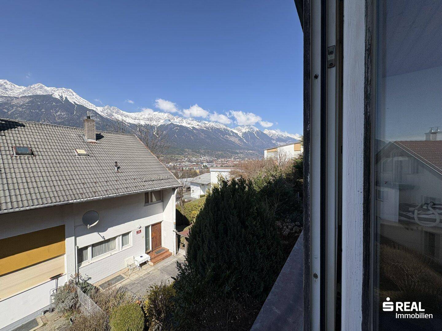 Panoramablick auf das eigene Haus und die umliegende Berglandschaft unter blauem Himmel.