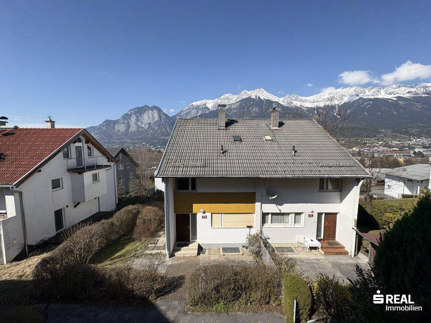 Gesamtansicht des Hauses mit Satteldach, umgebender Vegetation und majestätischem Bergblick.