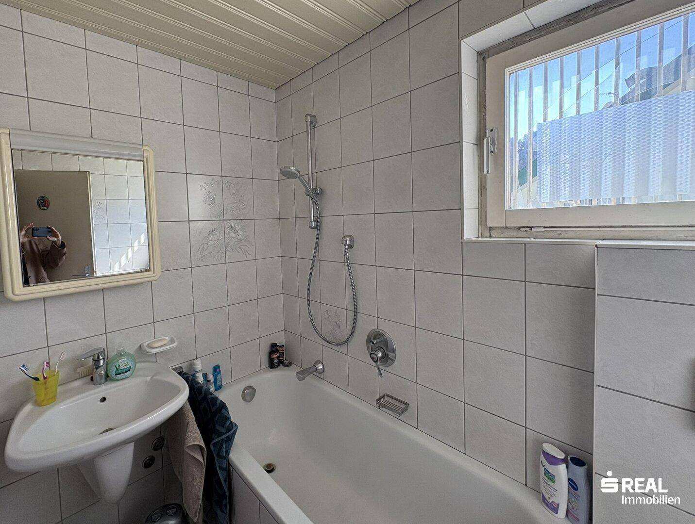 Badezimmer mit Badewanne, Duschfunktion, Waschbecken und einem Fenster für Tageslicht.