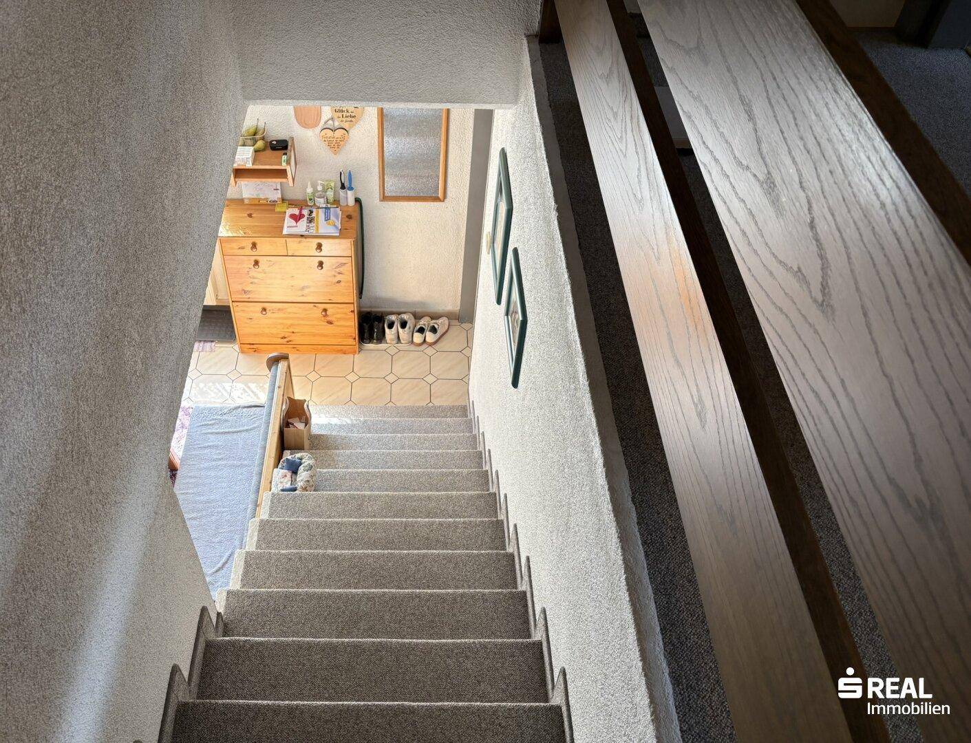 Treppenhaus mit Teppichboden, das in die untere Etage führt, und Holzgeländer.