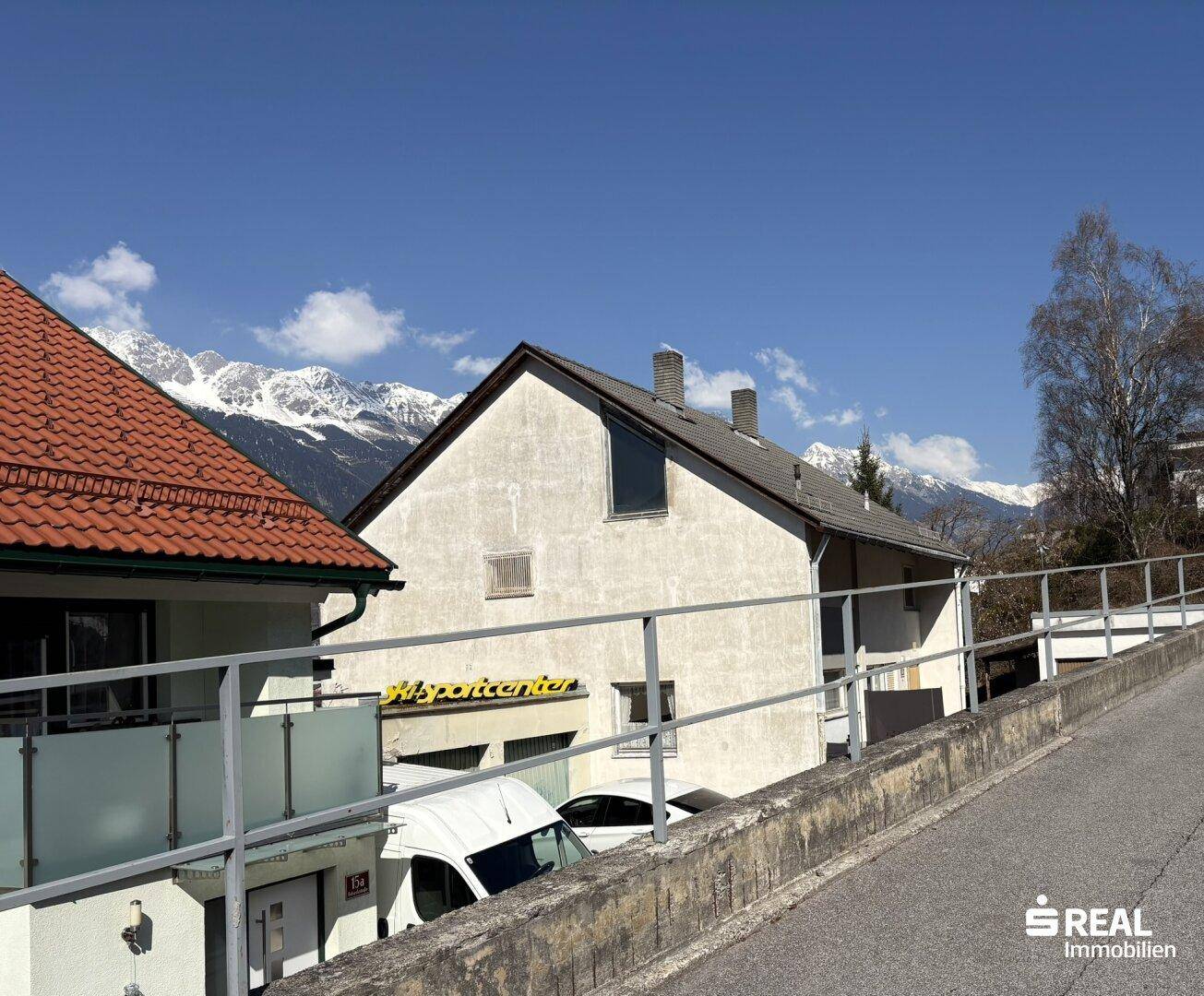 Seitenansicht eines Gebäudes mit Geschäftsbeschriftung und schneebedeckten Bergen im Hintergrund.