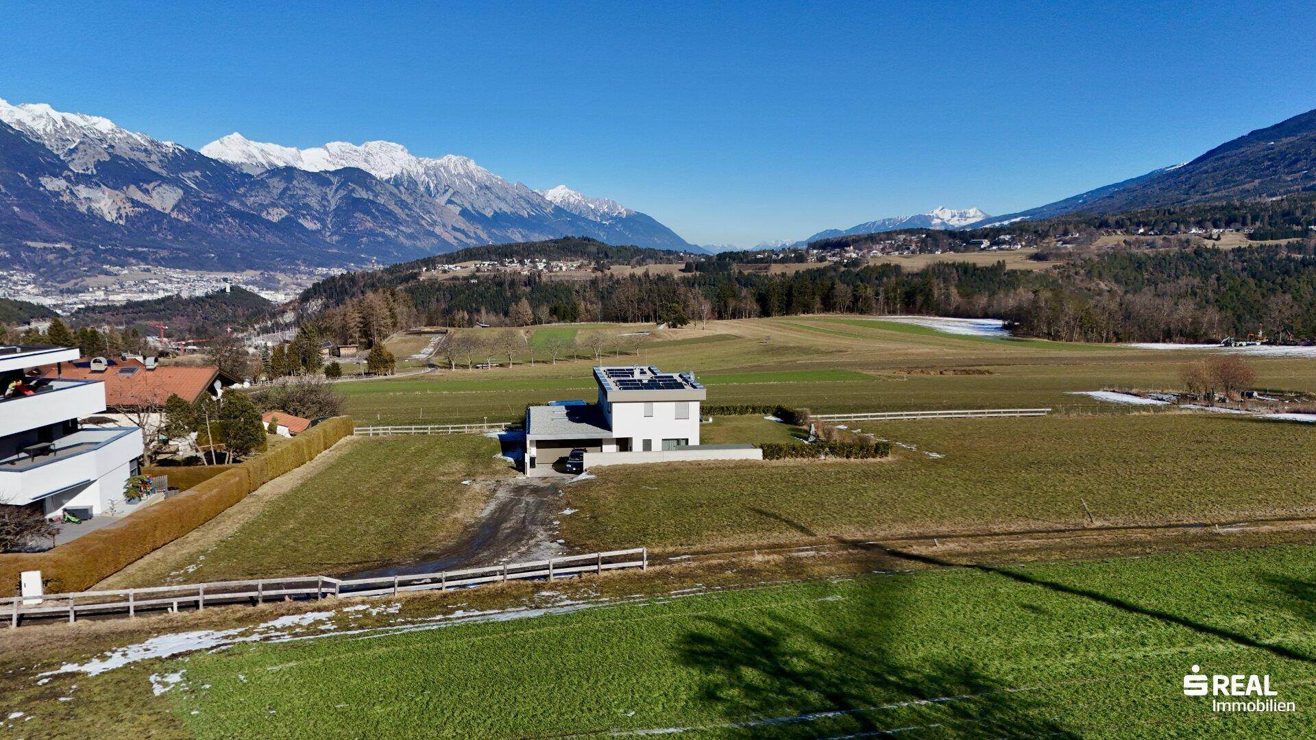 Luftaufnahme eines modernen Hauses mit Photovoltaikanlage in einer weiten Landschaft mit Bergpanorama.