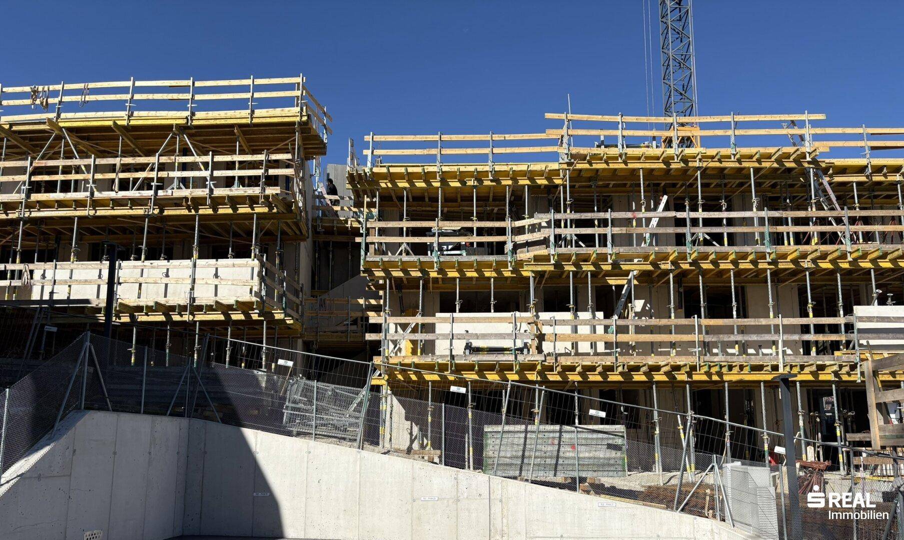 Detailansicht eines Neubaus im Rohbau mit umfangreicher Schalung und Gerüst unter blauem Himmel.