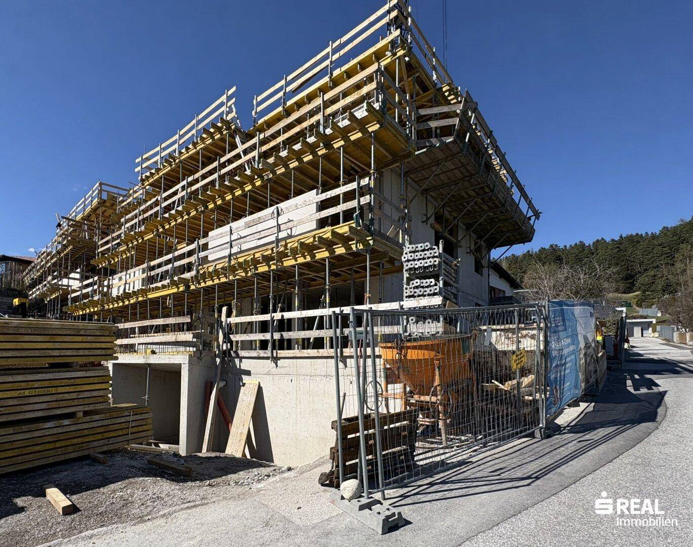 Neubauprojekt im Rohbauzustand mit Schalung und Gerüst, umgeben von grüner Landschaft.
