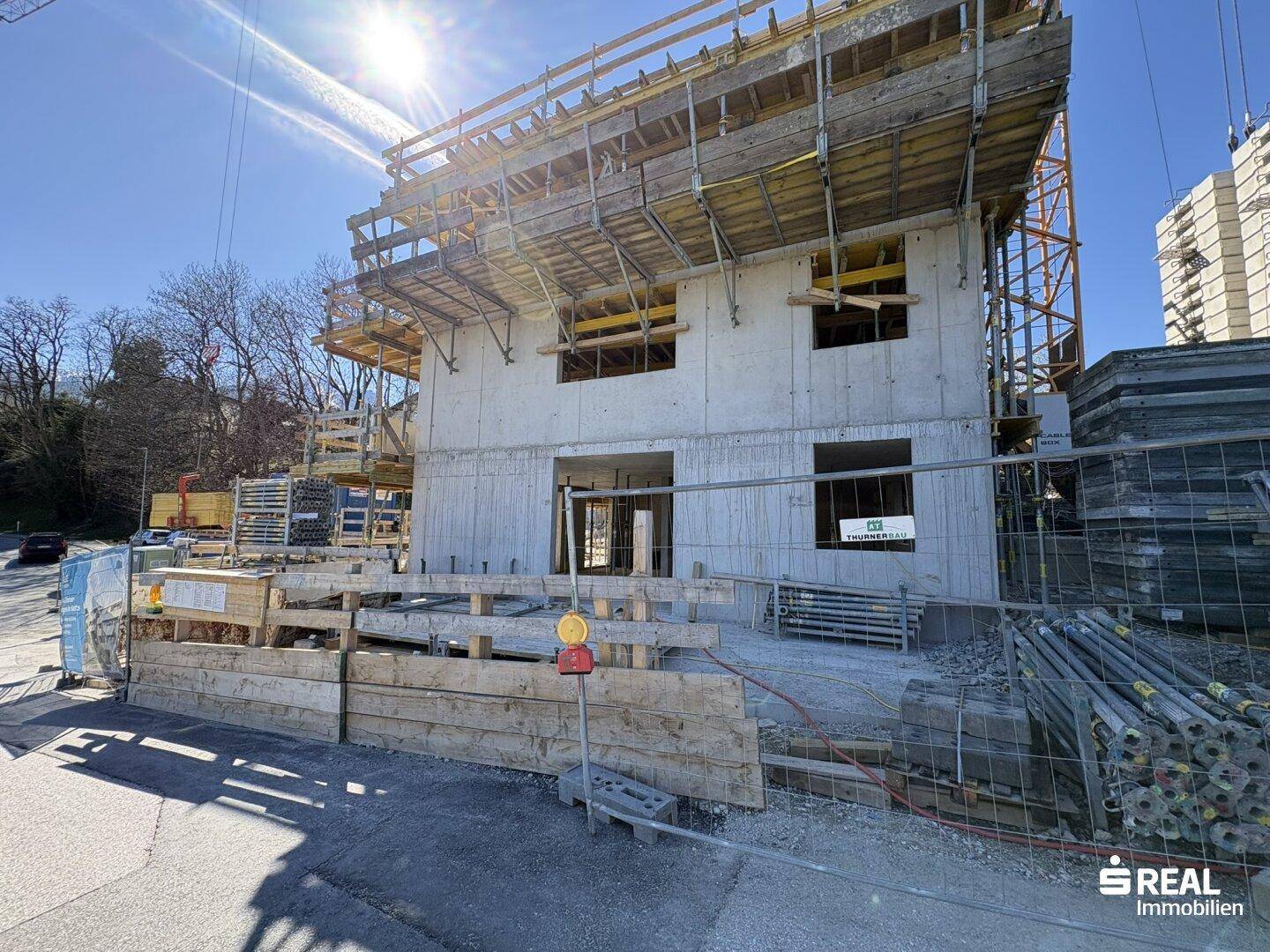 Im Bau befindliches Gebäude mit Betonfassade und Gerüst unter strahlendem Sonnenschein.