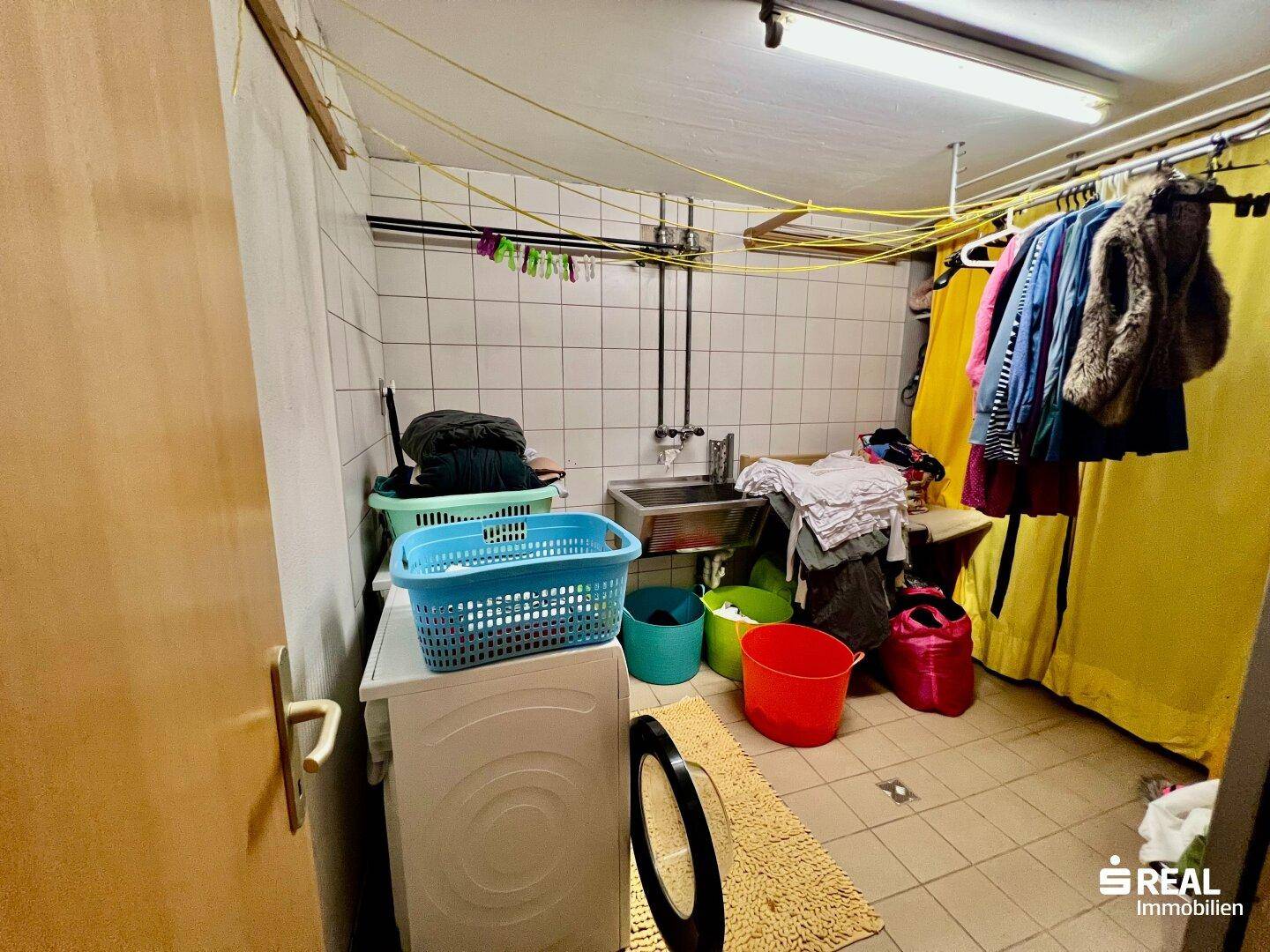 Praktischer Hauswirtschaftsraum im Keller mit Waschmaschine, Spülbecken und Wäscheleinen.