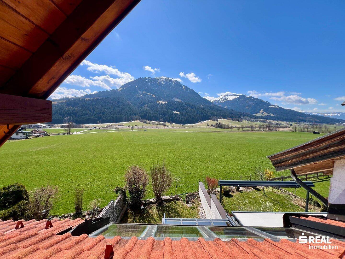 Weitläufiger Blick über grüne Felder und schneebedeckte Berge unter strahlend blauem Himmel.