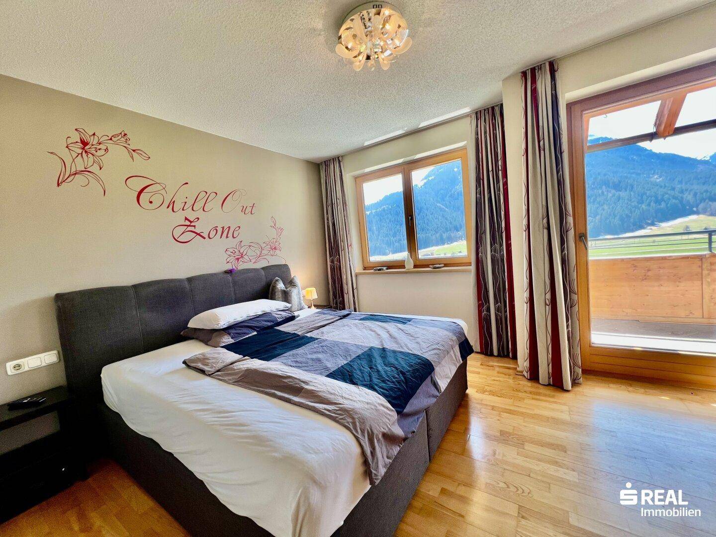 Geräumiges Schlafzimmer mit Holzboden, Zugang zum Balkon und herrlichem Bergblick.