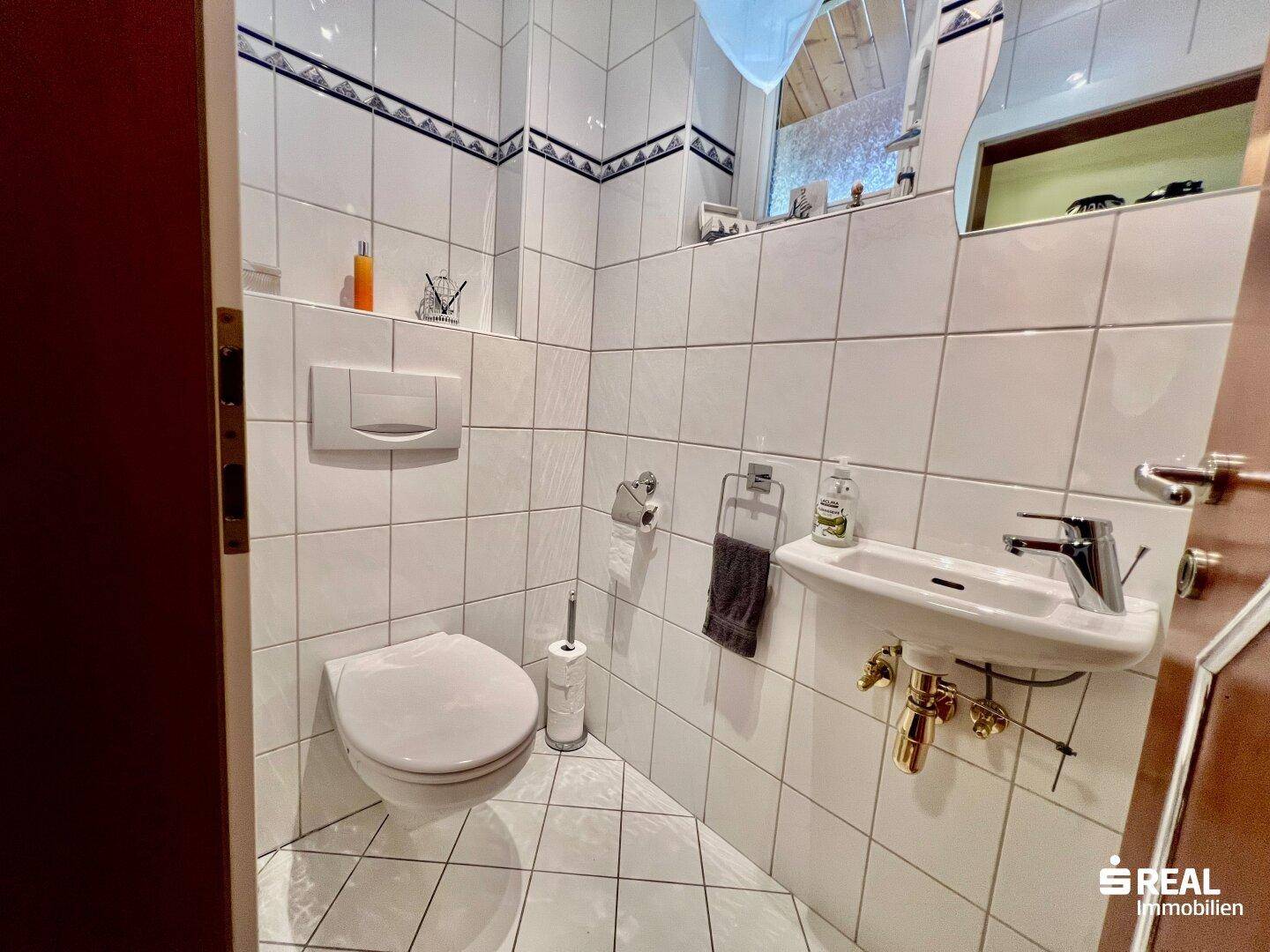 Kleines Gäste-WC mit Toilette und Waschbecken, gefliest in Weiß mit schwarzen Akzenten.