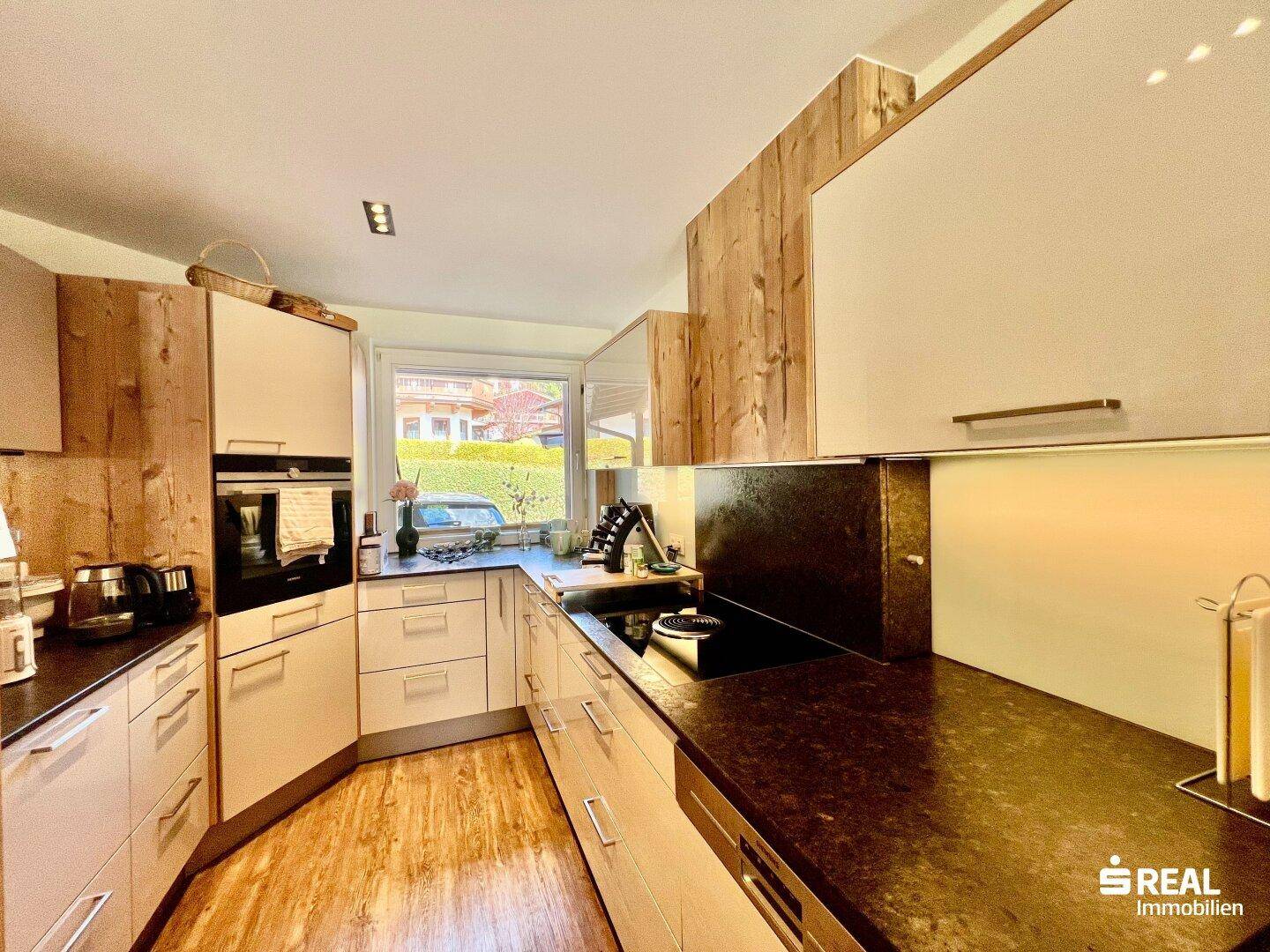 Moderne Küche mit Holz- und weißen Fronten, dunklen Arbeitsplatten und eingebauten Geräten.