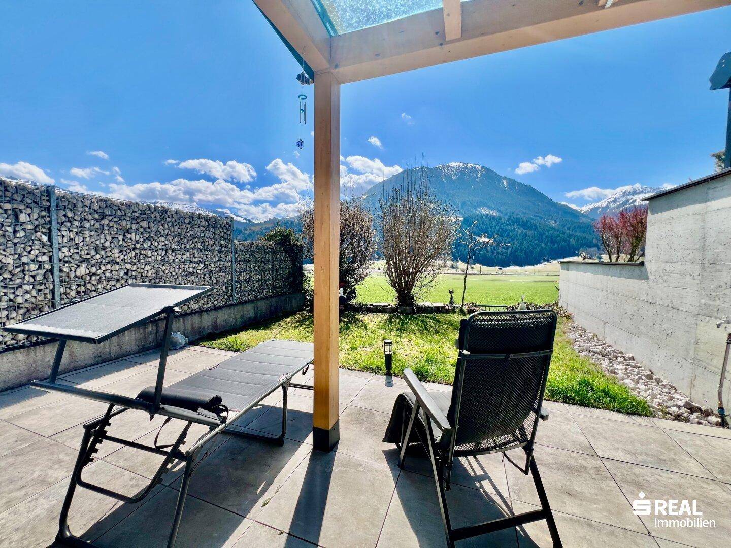 Sonniger Terrassenbereich mit Liegestühlen und Bergblick, teilweise überdacht von einer Holzpergola.