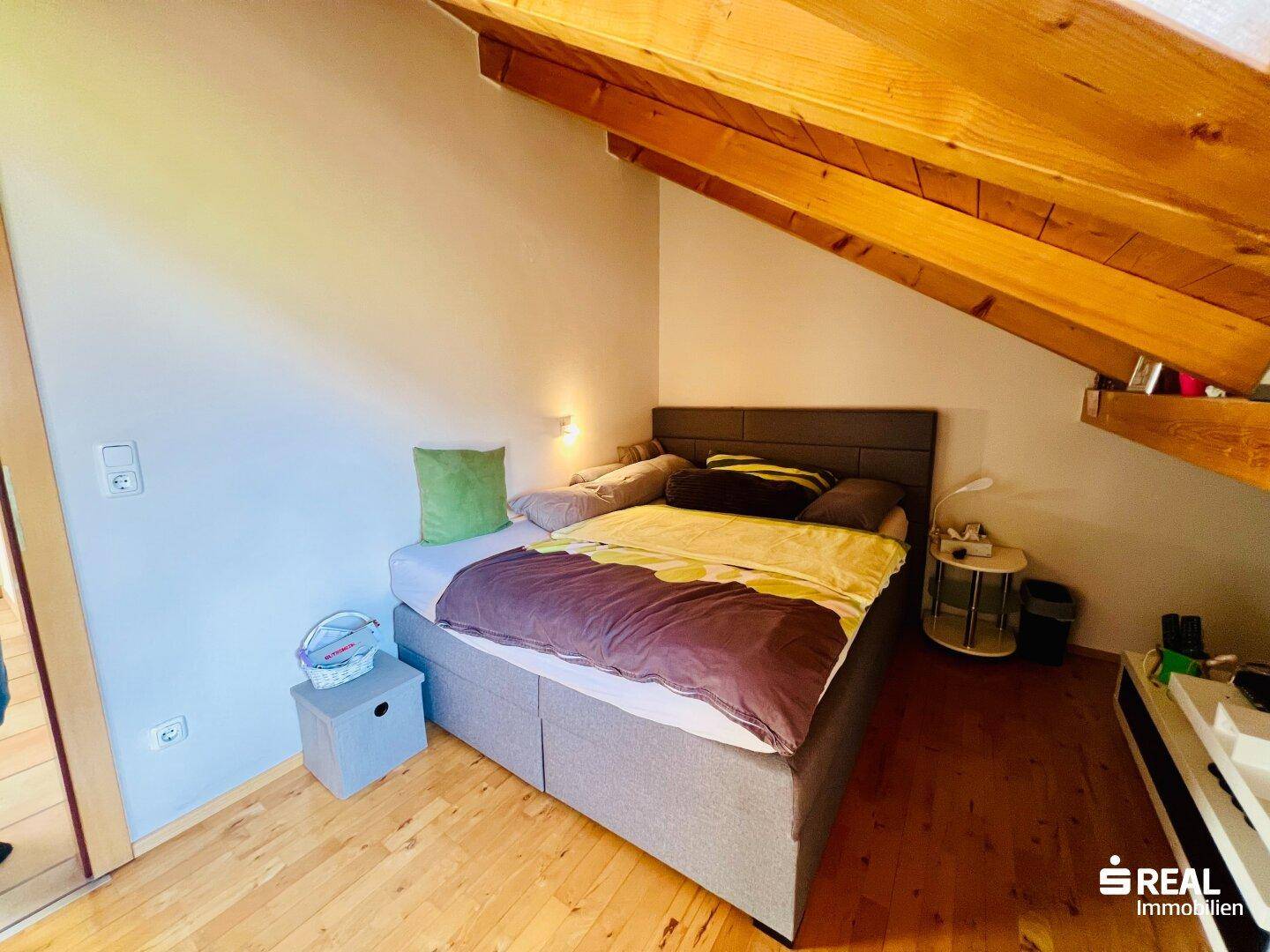 Helles Schlafzimmer im Dachgeschoss mit Holzboden und sichtbaren Holzbalken unter der Dachschräge.