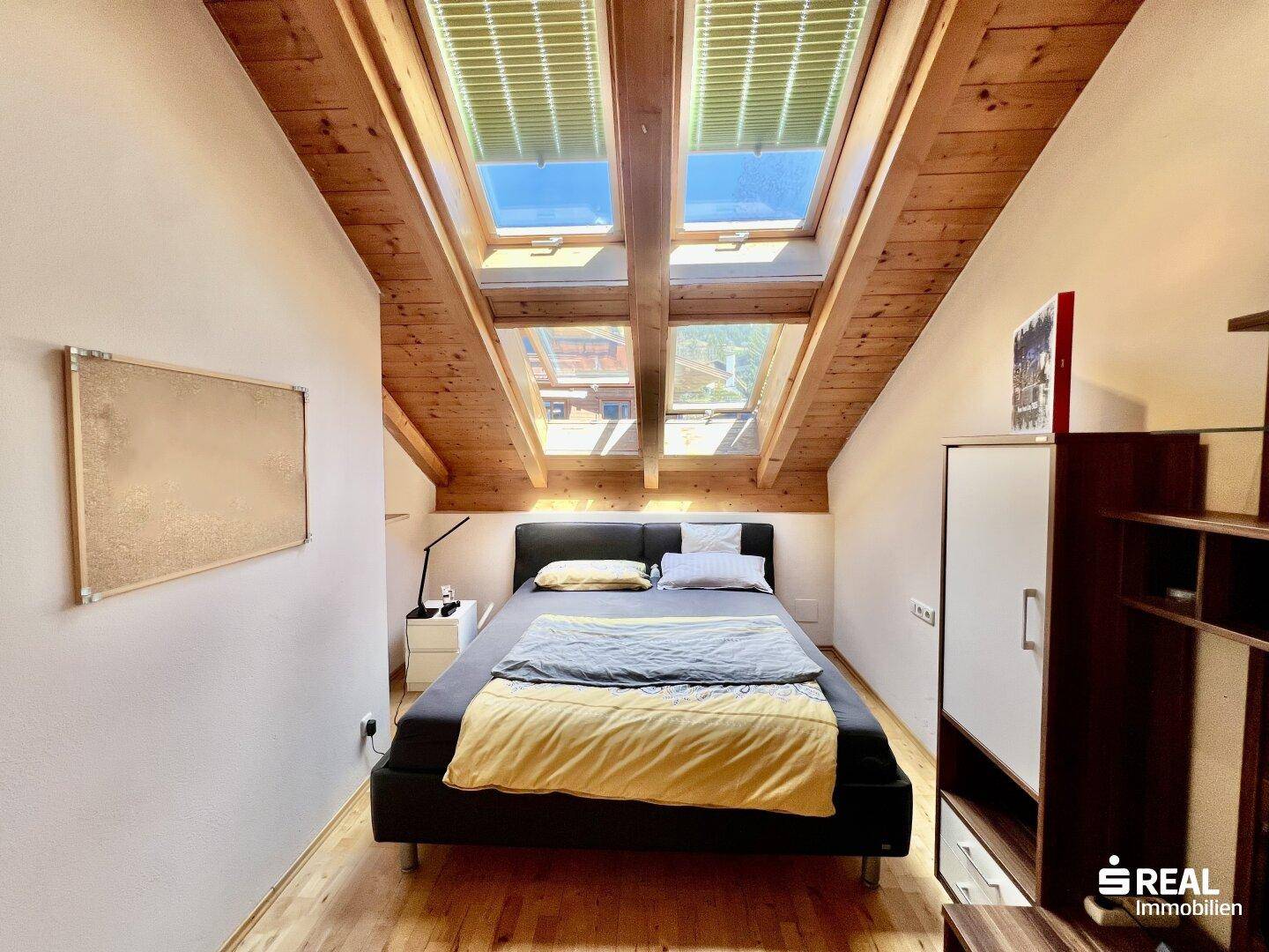 Dachschlafzimmer mit Holzboden, Bett und mehreren Dachfenstern für viel natürliches Licht.