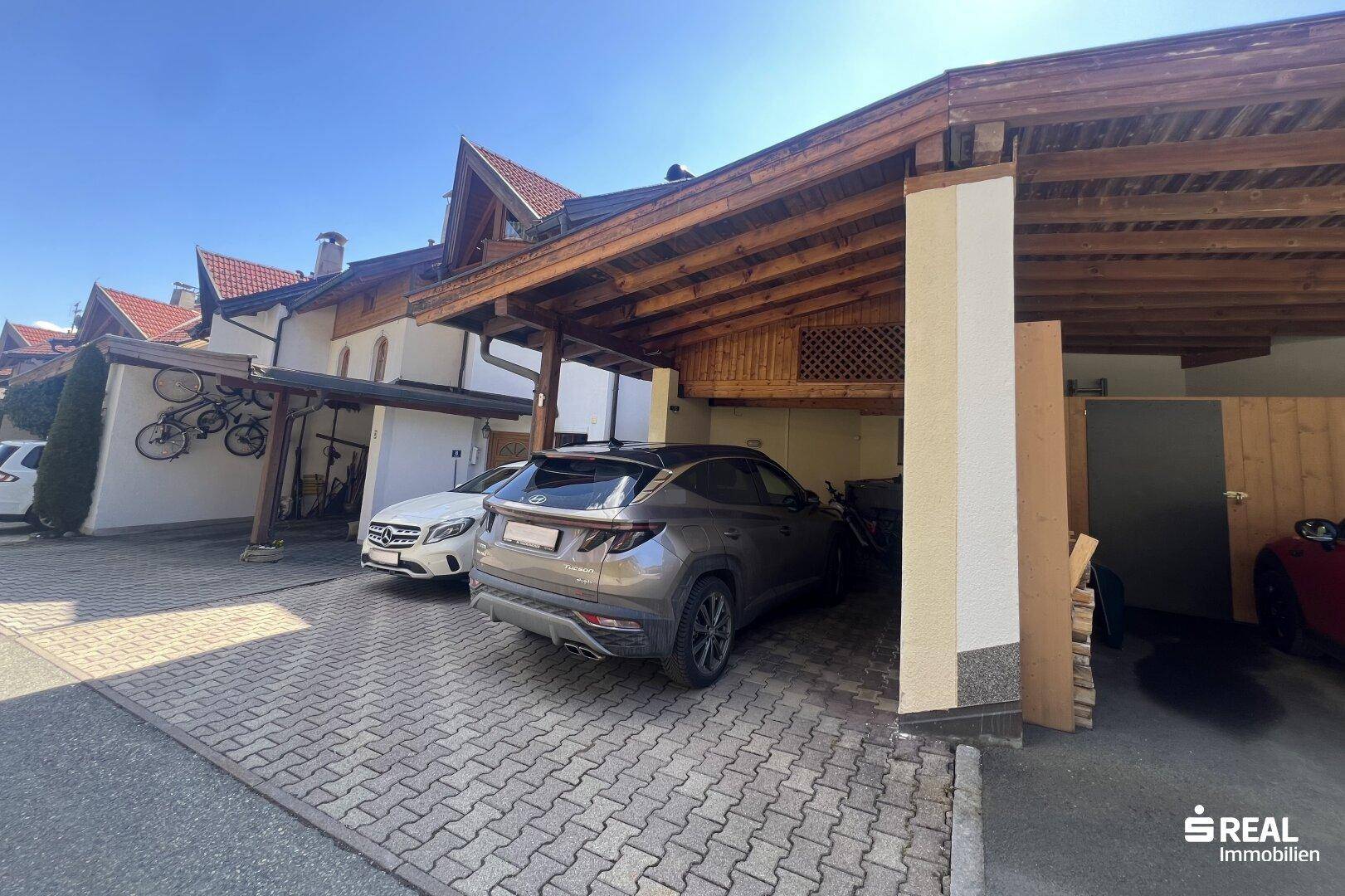Überdachter Carport mit Stellplätzen für Fahrzeuge und gepflasterter Einfahrt.