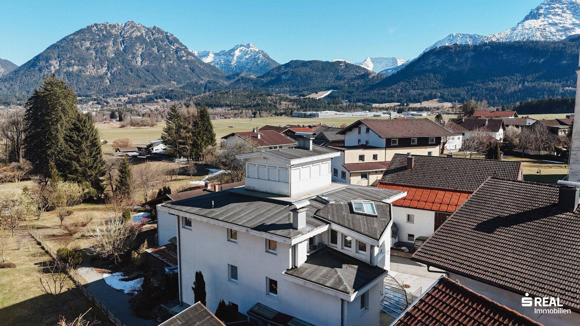 Ansicht des modernen Gebäudes mit Flachdach und umliegender Naturkulisse der Alpen.