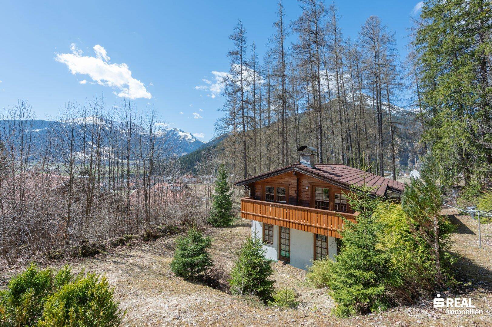 Panoramablick auf das Holzhaus in einer bewaldeten Umgebung mit weitreichender Aussicht auf die Berge.
