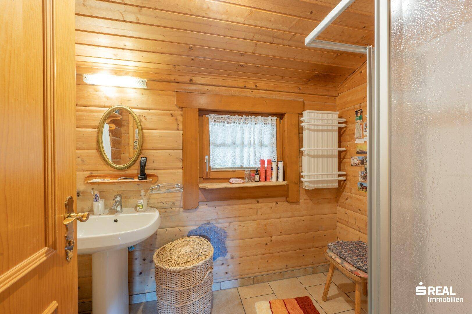 Badezimmer mit Holzvertäfelung, Fliesenboden, Waschbecken und Fenster für Tageslicht.