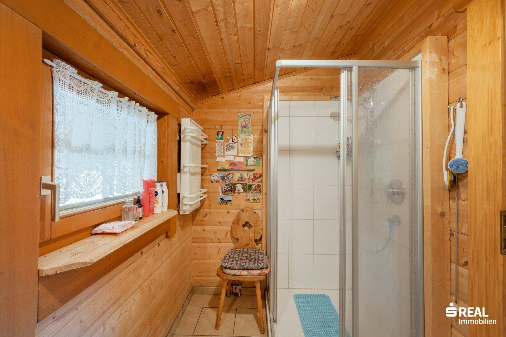 Duschbereich im Badezimmer mit Fliesen und Holzvertäfelung, hell und funktional gestaltet.