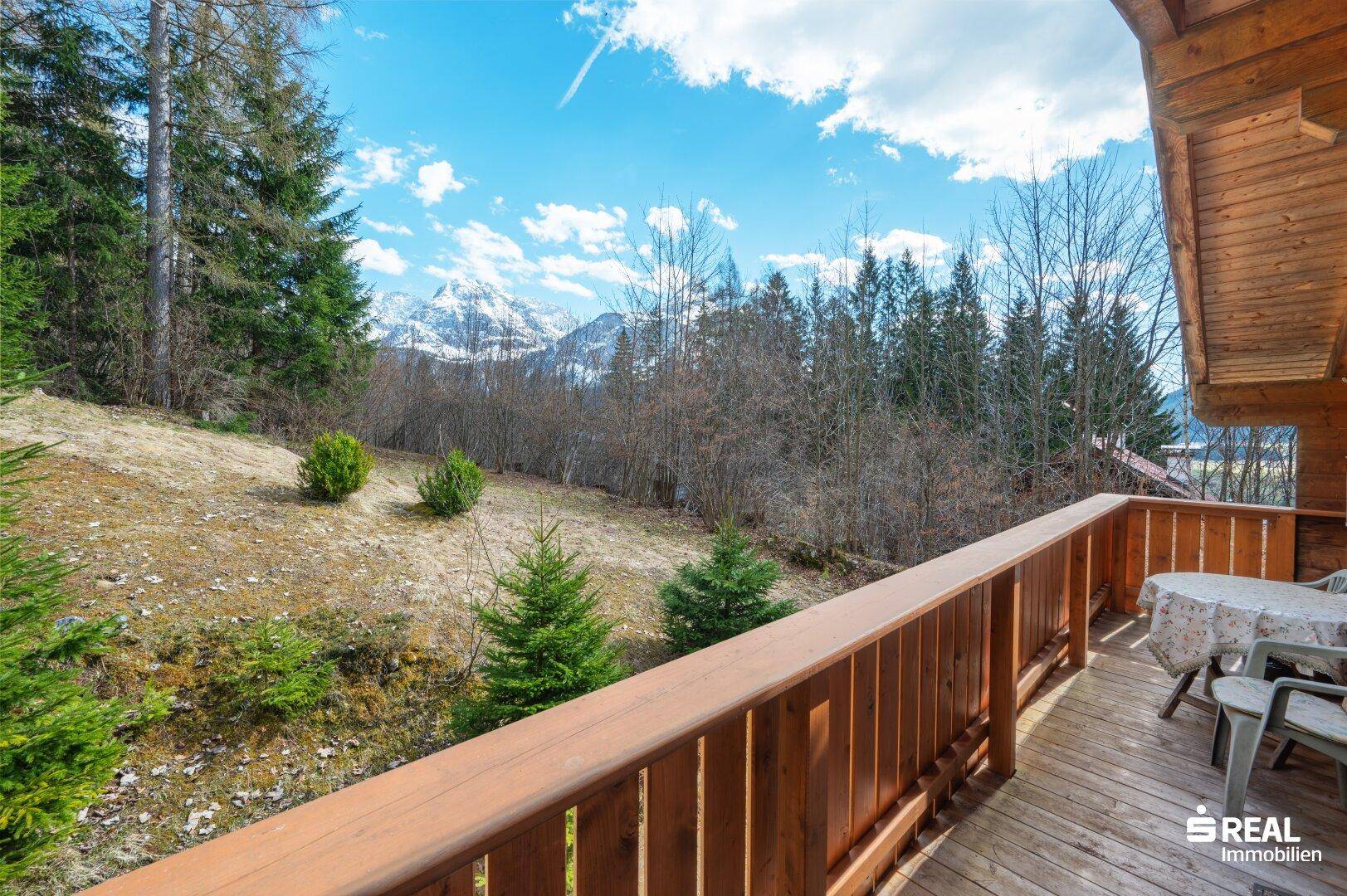 Sonniger Holzbalkon mit Sitzgelegenheiten und weitem Blick auf die umliegende Berglandschaft.