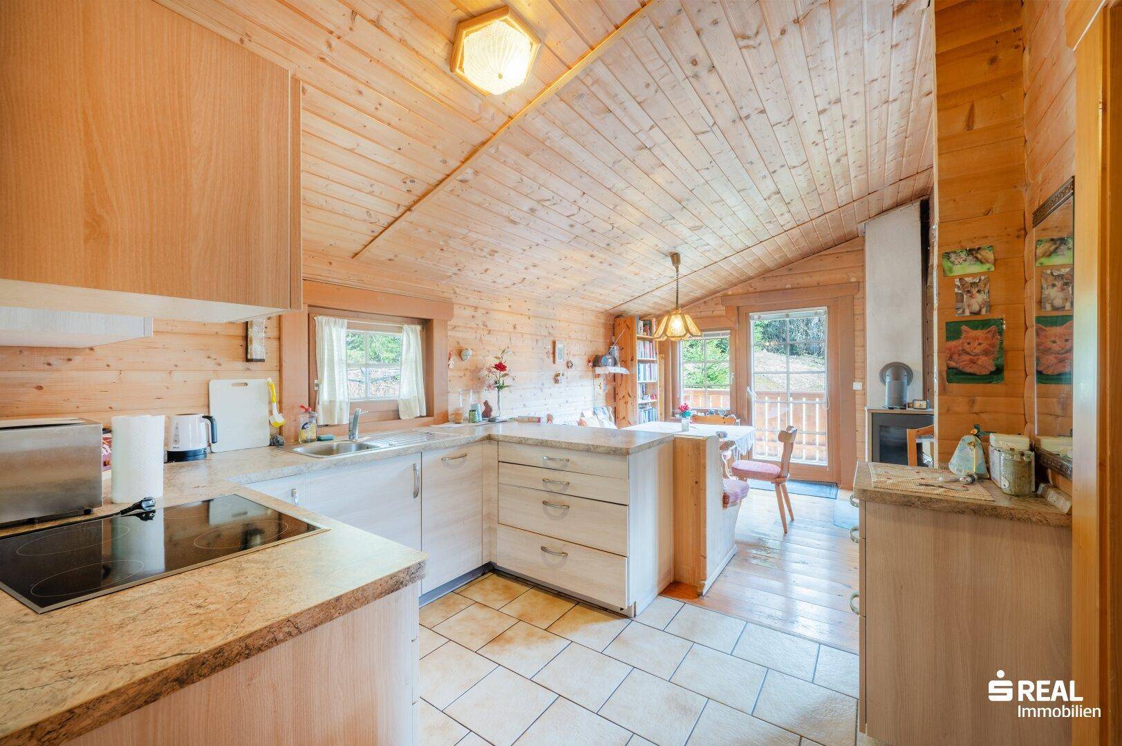 Gemütliche Holzküche mit Fliesenboden, Einbauküche und Essbereich mit Blick ins Grüne.