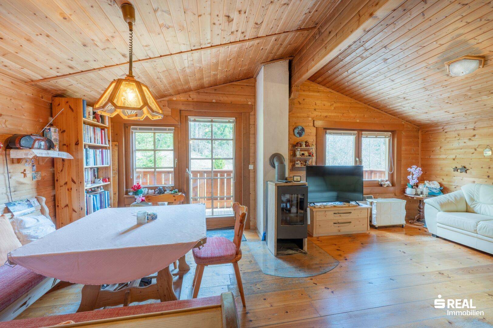 Heller Wohn- und Essbereich mit Holzboden, Kaminofen und Zugang zum Balkon.