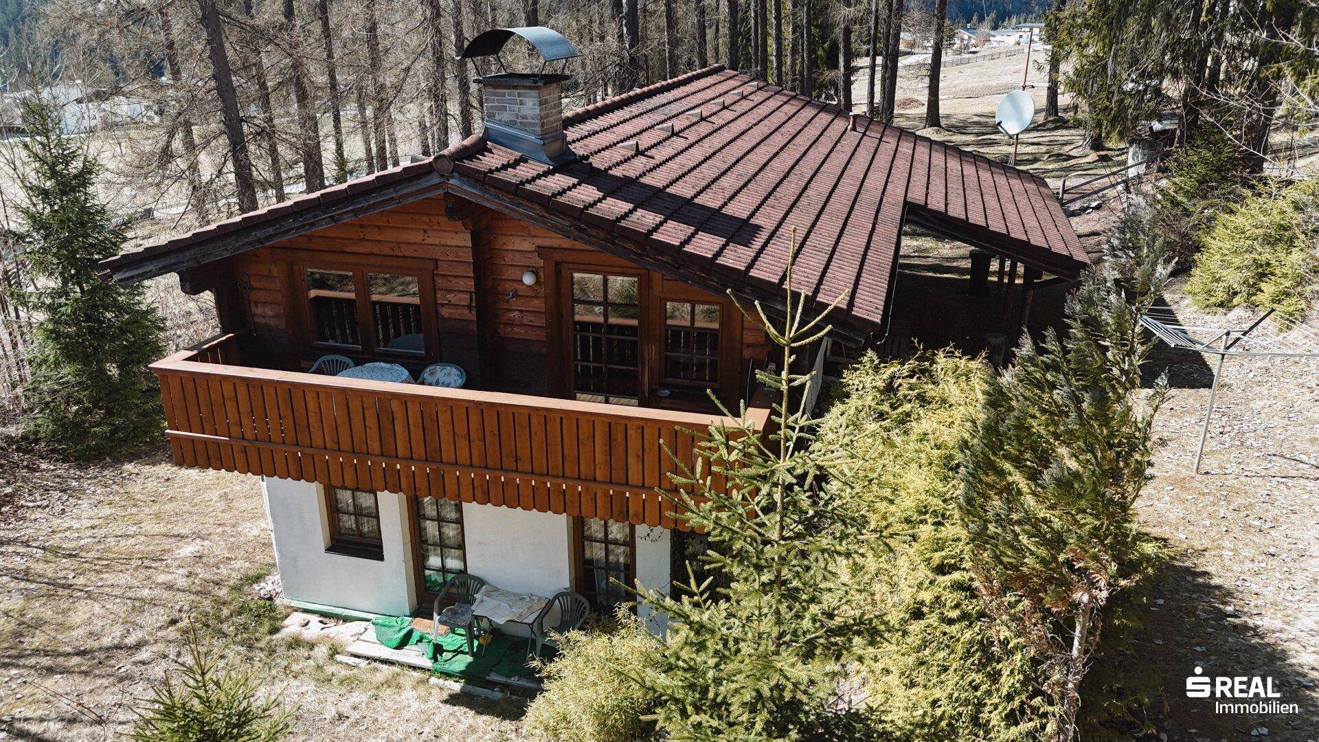 Vogelperspektive des Holzhauses mit Balkon und umliegender Natur, ideal für Ruhesuchende.