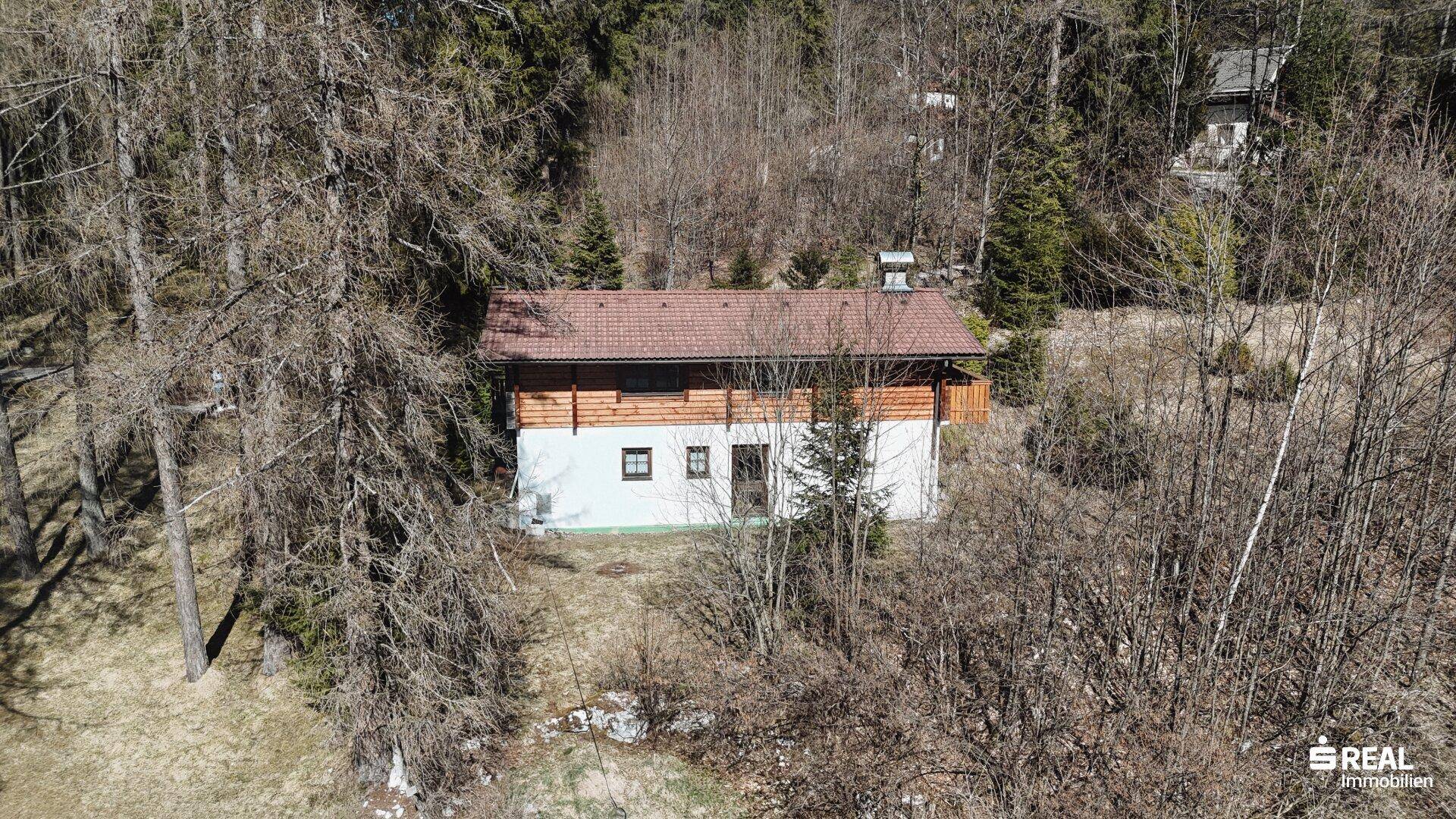 Luftaufnahme des Holzhauses, eingebettet in eine bewaldete Landschaft mit weitem Blick.